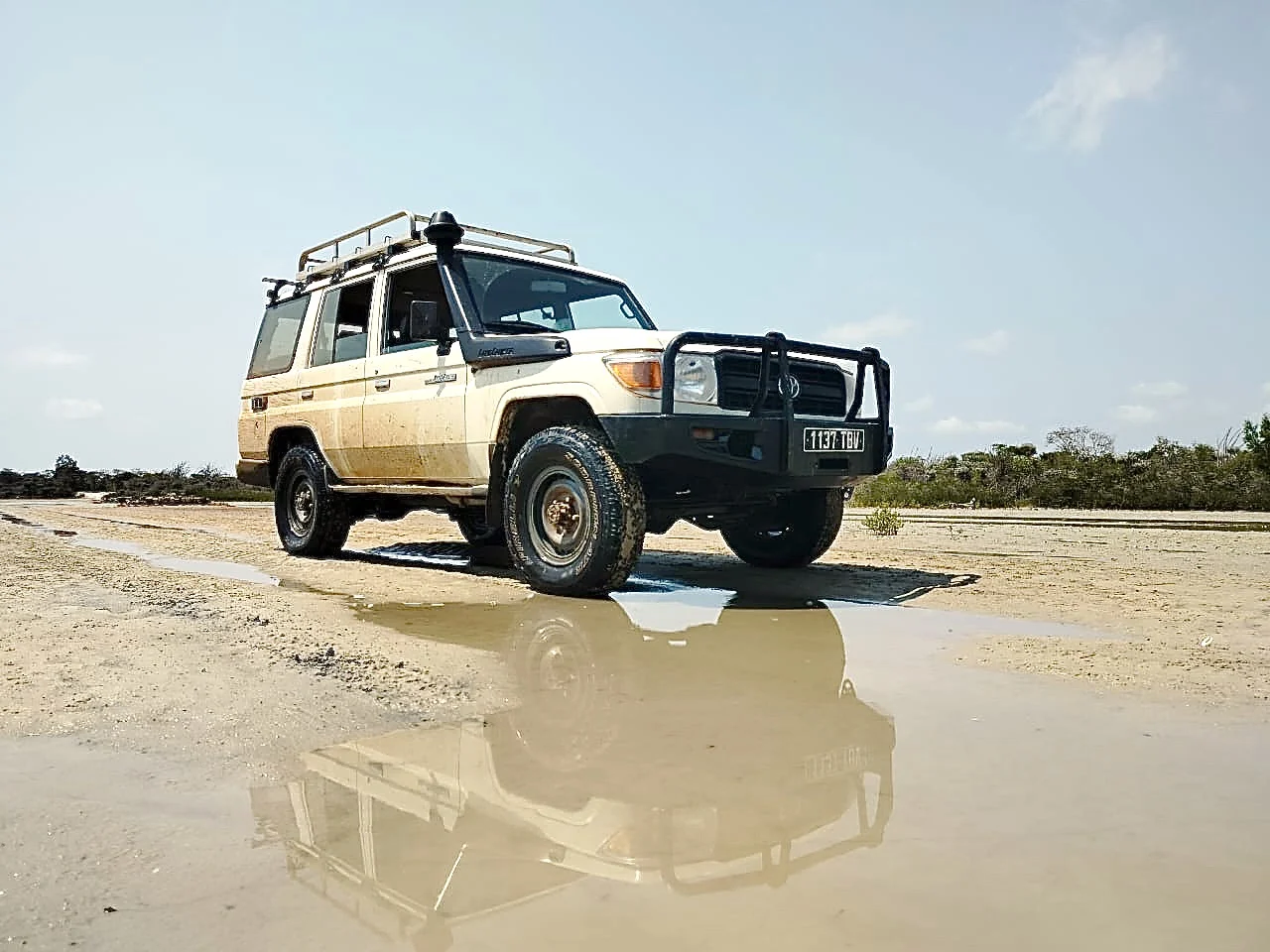 Een van onze Toyota Land Cruisers op een zandpiste, weerspiegeld in een plas