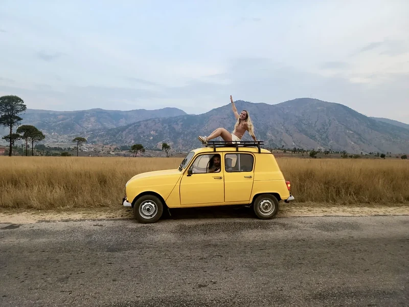 A traveller on the roof of the yellow Renault 4 Sinpar below the mountains