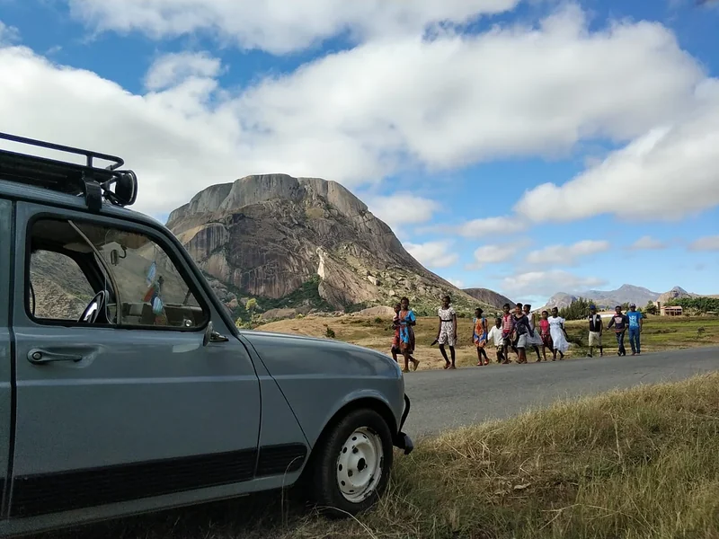 Villagers walk past a grey Renault 4 below a granite dome on the RN7