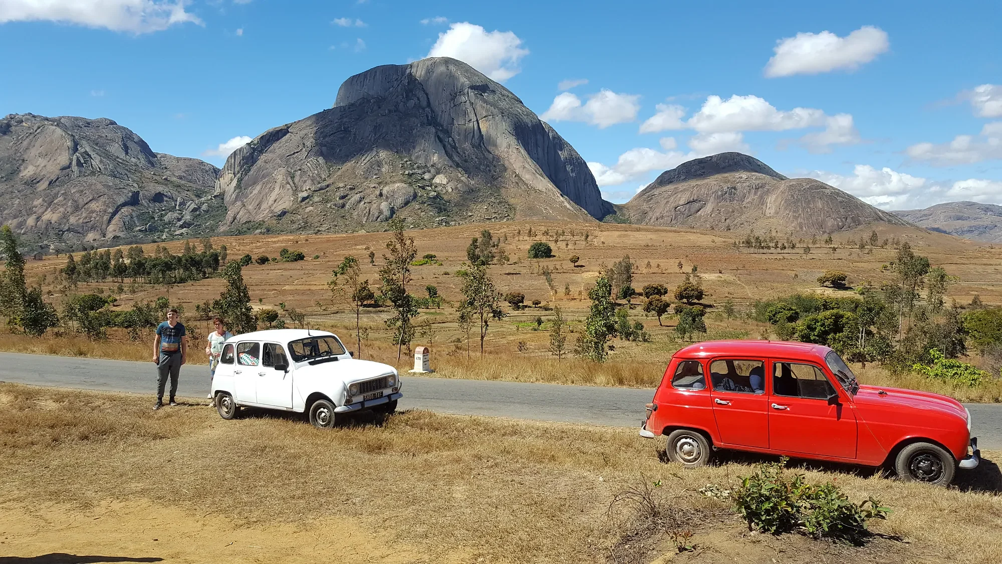 A white and a red Renault 4 on the road below granite peaks in the highlands of Madagascar