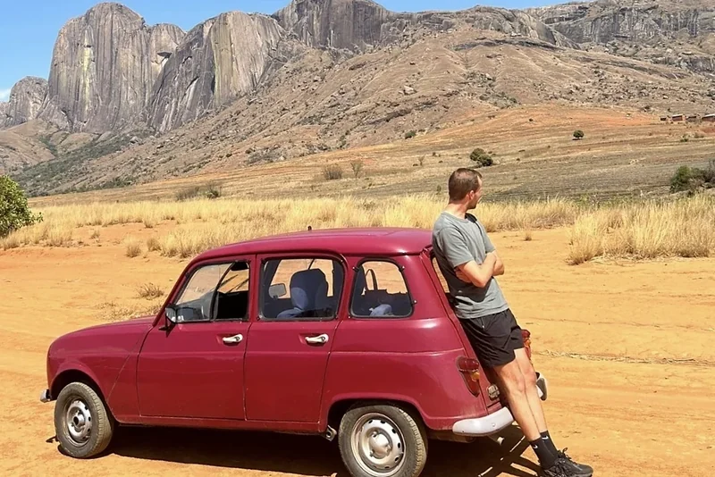 A traveller leans on a red Renault 4 below the granite peaks of Andringitra