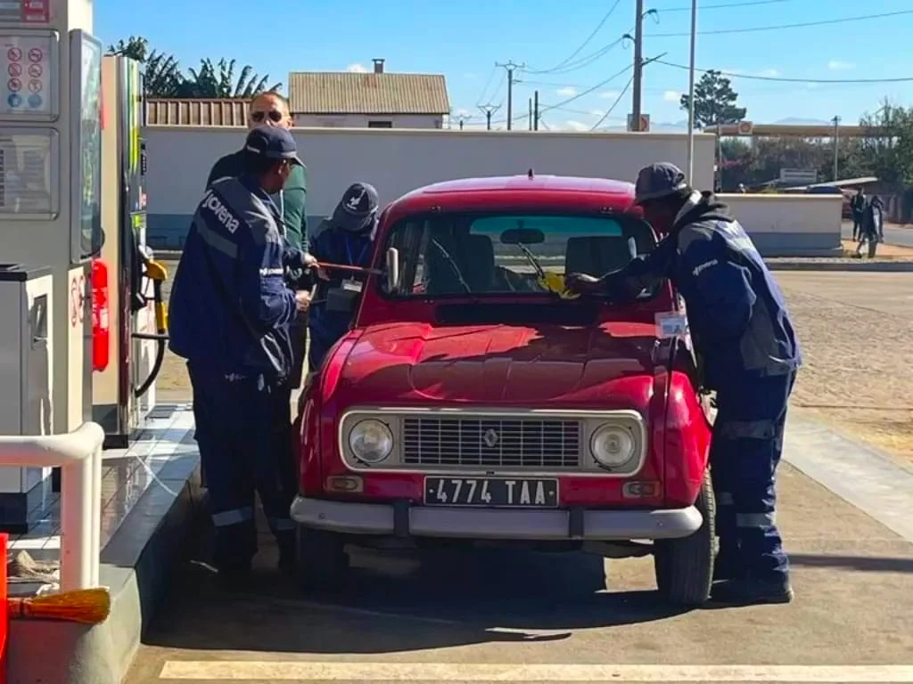 Station attendants check the oil and clean the windscreen of a red Renault 4