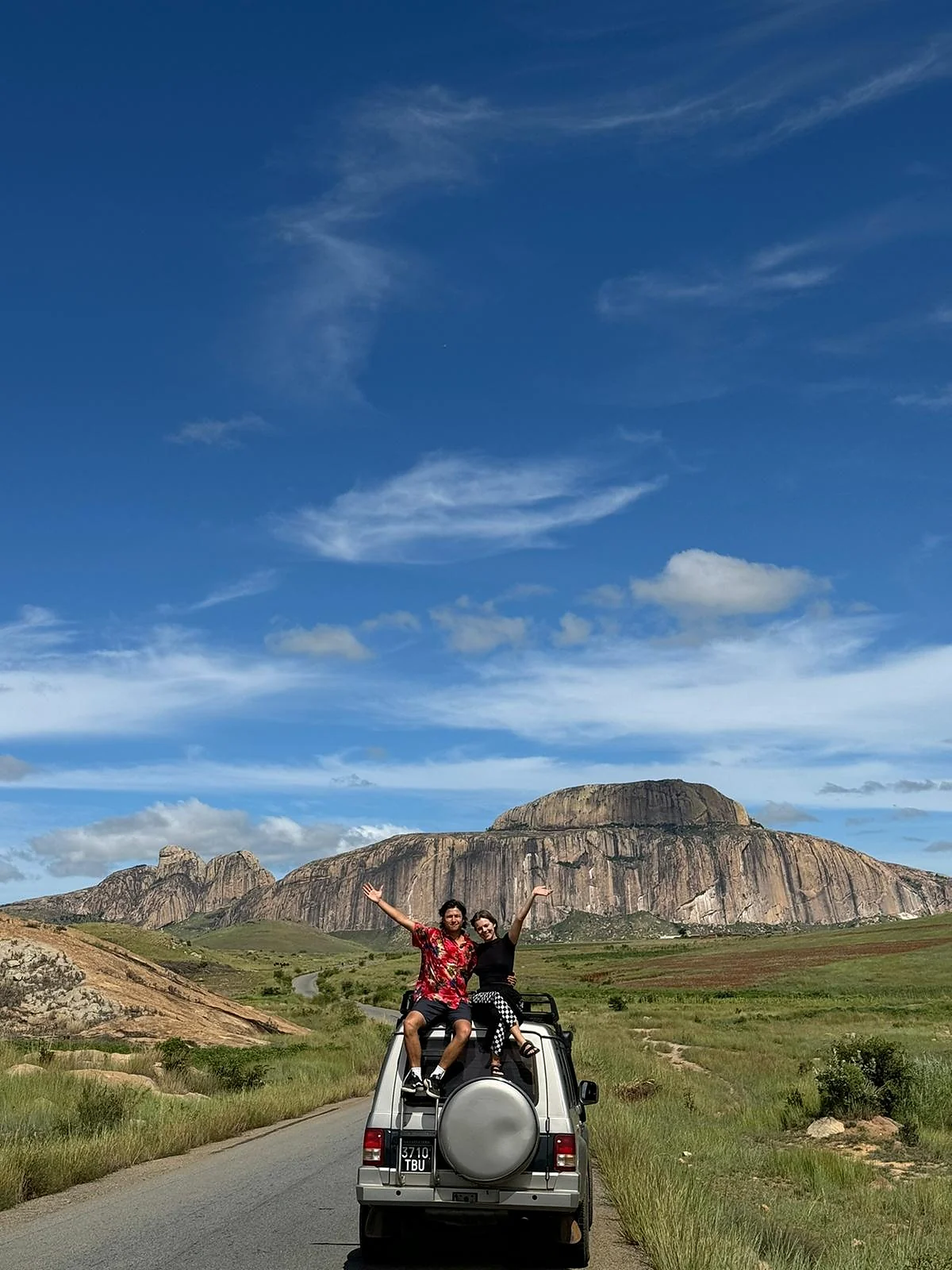Deux voyageurs sur le toit de leur 4x4 sur la RN7, au pied d’un dôme de granit